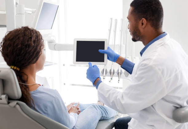 istock Black guy dentist showing patient digital tablet with blank screen 1253025153