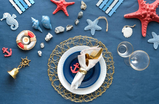 istock Contemporary nautical table setting with sea decorations on classic blue linen textile. Plates, golden cutlery, utensils. Top view, Columbus Day or Summer birthday lunch table, blue white with red. 1253025446