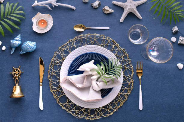 istock Contemporary nautical table setting with sea decorations on classic blue linen textile. Plates, golden cutlery, utensils. Top view, Columbus Day, Summer birthday lunch table, blue, white and green. 1253025562