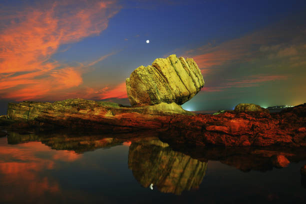 A pool of water trapped in a depression within a rock formation reflects the sky, showing storm clouds rolling in at sunset.