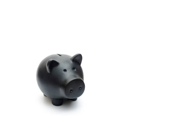 A dark piggy bank with eye patches stands before a black wall.