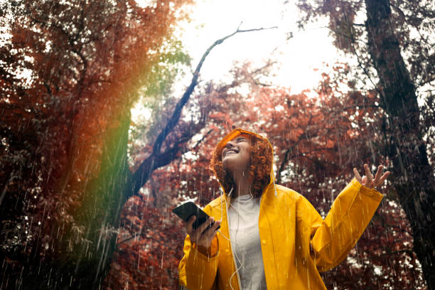 glückliche junge frau im regenmantel an einem regnerischen tag hören musik blick auf regenbogen - telephone nature mobile phone autumn stock-fotos und bilder