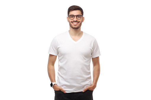 Young man standing with hands in pockets, wearing glasses and blank white tshirt with copy space, isolated on studio background