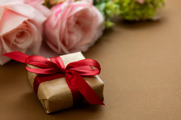 istock Gift box with red bow and pink roses, brown background. 1253036851