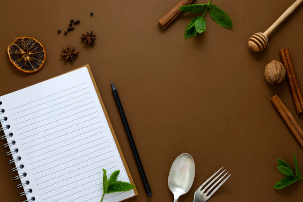 istock Food mock up. Open notebook, food condiments, fork and spoon. Anise star, cinnamon sticks, mint leaves. Brown background. 1253036867