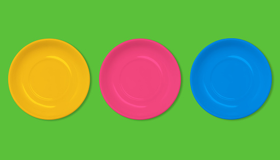 Orange, red and blue plate on a green background. Colorful empty food plates. Fashionable creative and summer style. Minimal design. Flat layout, top view.