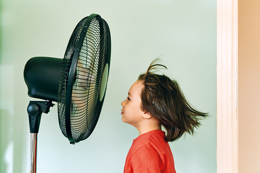 Cute child is front of electric fan on hot summer day