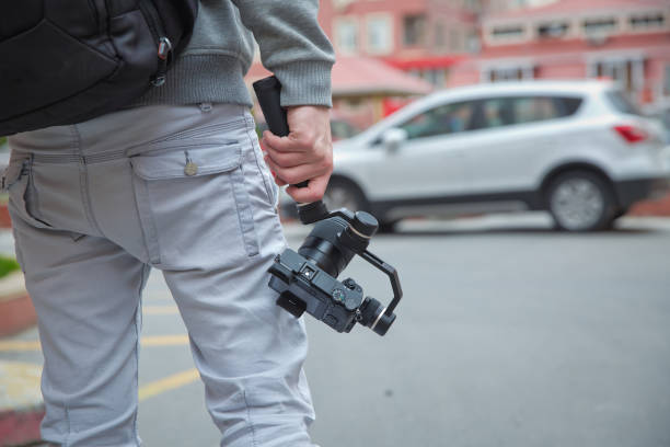 istock An unidentified man holding gimbal a camera stabilizer . Man holding gimbal stabilizer outdoor. Gimbal Operator with black equipament - Stabilizer and camera filmmaking 1253041178