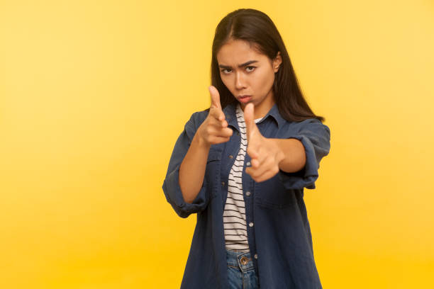 I'll shoot you! Portrait of purposeful dangerous girl in denim shirt shooting to camera with finger pistols I'll shoot you! Portrait of purposeful dangerous girl in denim shirt shooting to camera with finger pistols, threatening to kill, gesturing weapon. indoor studio shot isolated on yellow background shooting a weapon photos stock pictures, royalty-free photos & images