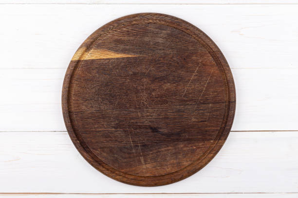istock Brown round cutting board on a white wooden background. View from above. 1253043931