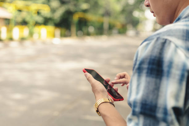 Young Asian man holding cell phone and waiting for Uber taxi.