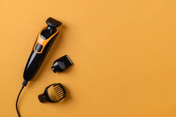 Electric black hair clipper or trimmer on a textured yellow background. Barber professional tool for cutting hair. Haircut at the hairdresser or at home. Copy space. Top view.