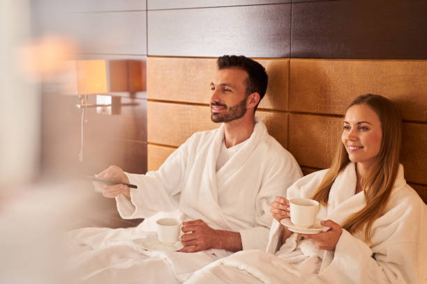 istock Joyful couple watching tv with hot drinks in bed 1253056686
