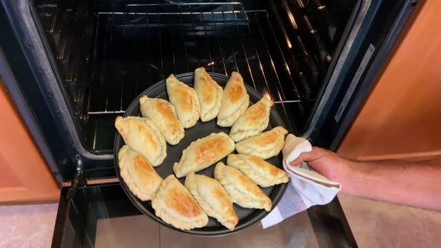 A taking argentinean empanadas out of the oven, pastry concept and home cooking.
