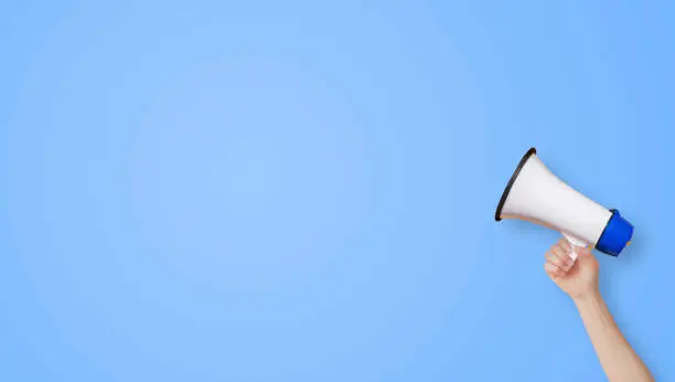 Photo of Female hand holding megaphone for announcement and advertisement with blank blue background.