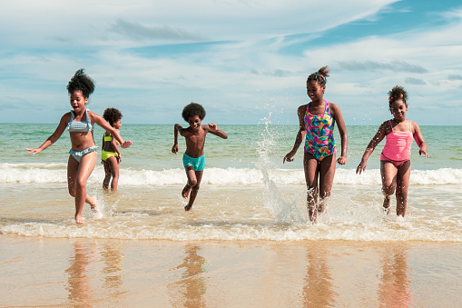 Group of African American boy and girls in swimsuit run on the beach. Concept of friendship, childhood, and summer vacation and travel after covid 19 lock down