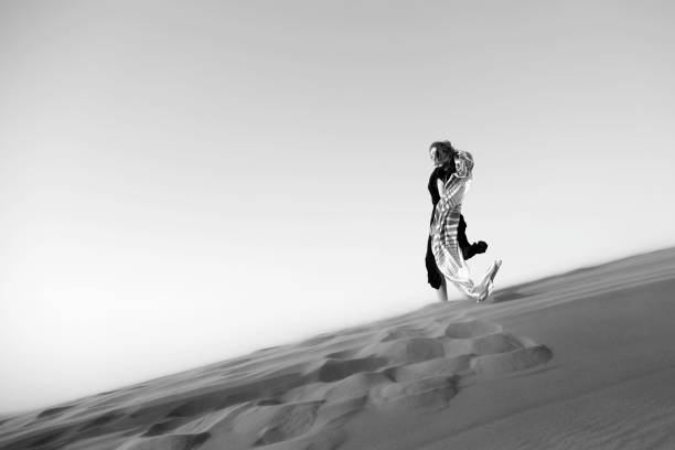 Caucasian woman in a black dress descends from a mountain in the desert. Black and white shot