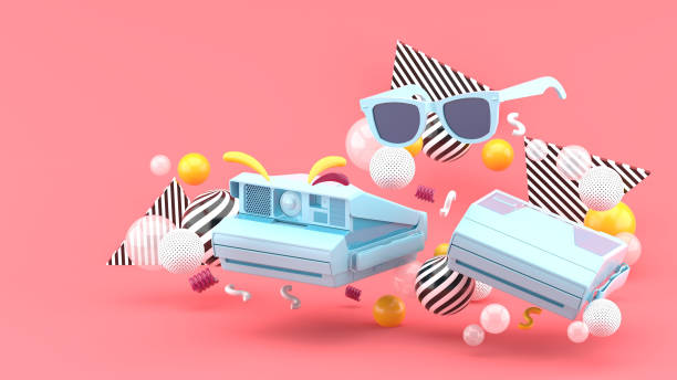 istock Polaroid camera and blue glasses surrounded by colorful balls on a pink background.-3d render. 1253073330