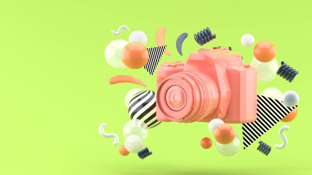 緑色の背景にカラフルなボールに囲まれたピンクのカメラ. - sensory perception flash ストックフォトと画像