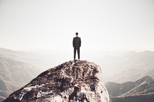 Businessman staring into the distance from mountain cliff looking for solution. Business and challenge concept.