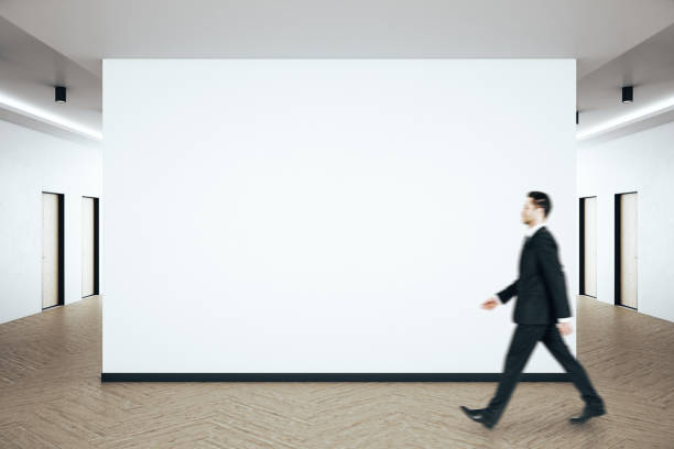 istock Businessman walking in clean hall interior with blank white wall 1253081583