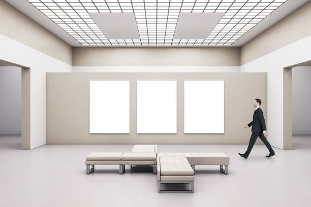 istock Businessman walking in modern gallery interior with empty billboard 1253081672