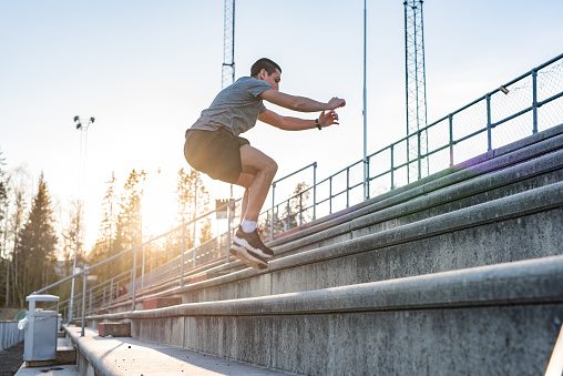 Well trained man exercising on stadium stairs at sunset.