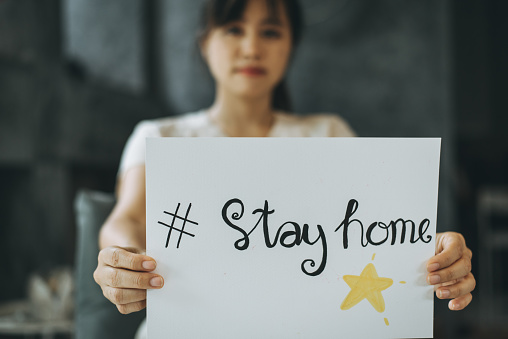 Woman staying at home and holding paper with hashtag Stay home.