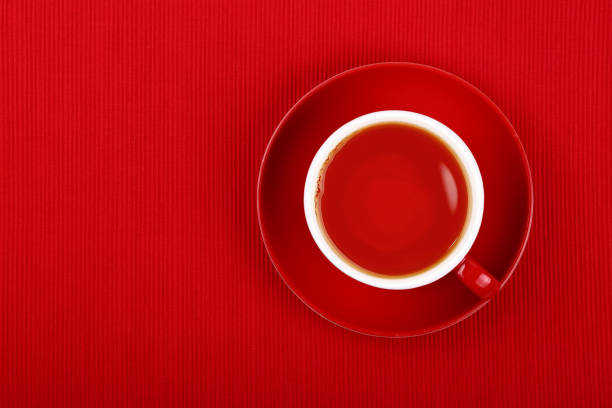 Close up one cup full of black or fruit tea on saucer over red tablecloth, elevated top view, directly above