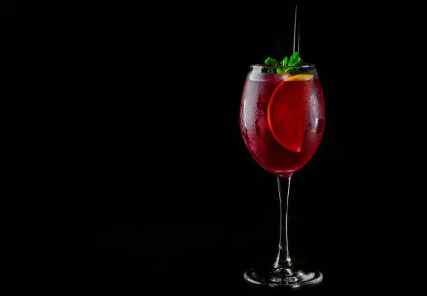 Cold sangria wine in a wine glass with reflection on black background