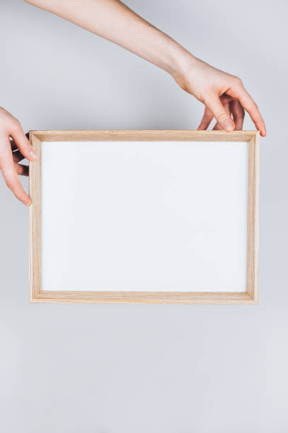 istock Woman hands holding a wooden frame with a clear blank white background. 1253098689
