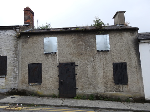Derelict house on a sloped street with windows and door boarded up in Drogheda, County Louth, Ireland.