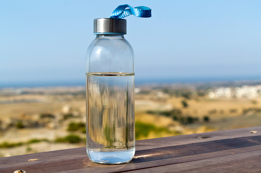 Close-up of glass bottle of water on wooden picnic table with blurred panoramic view on background