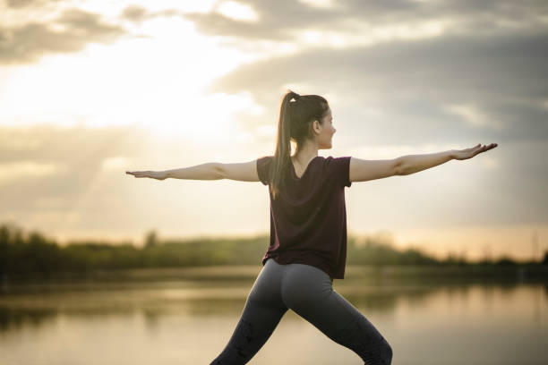 istock Young attractive woman in Warrior two pose on lake docks 1253108896