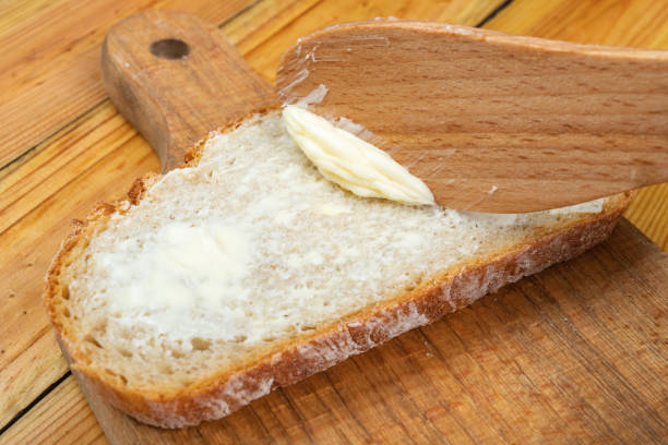 istock Butter spreading on fresh bread. Bread in the home kitchen. Dark background. 1253110971