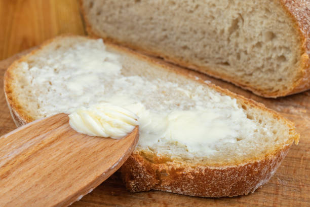istock Butter spreading on fresh bread. Bread in the home kitchen. Dark background. 1253111042