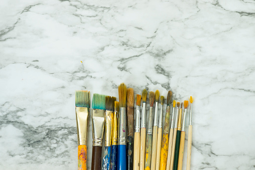 Small assorted group of artist's paintbrushes in various sizes and shapes lined up together in an uneven row together on a bright marble background.