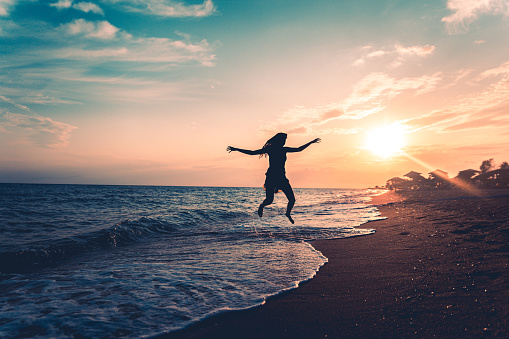 Silhouette of a woman jumping on the beach with outstretched arms at sunset
