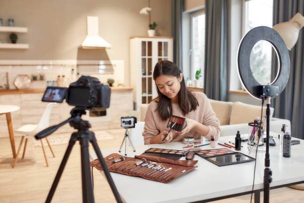 istock Drawing attention. Asian female blogger showing cosmetic products while recording a tutorial video for her beauty blog using camera at home 1253123969