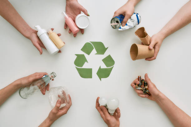 istock Go green with recycling. Top view of many hands holding different waste, garbage types with recycling sign made of paper in the center over white background 1253127522
