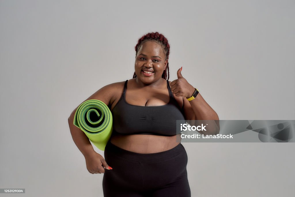 Every Body Beautiful Cheerful Plump Plus Size African American Woman In  Sportswear Showing Thumbs Up Holding Green Yoga Mat For Fitness In Studio  Over Grey Background Stock Photo - Download Image Now 