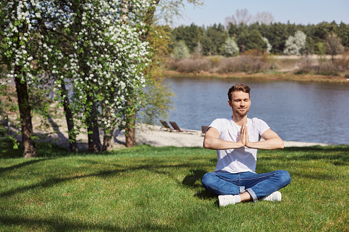 Handsome relaxed male training yoga while holding palms pressed together
