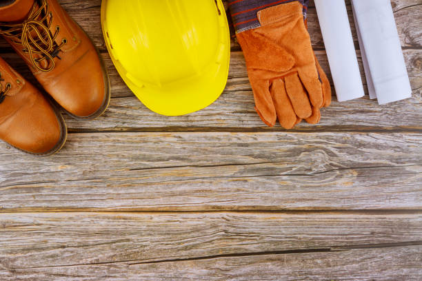 istock Industry worker protective workwear safety boots leather gloves yellow hard hat on architects working with blueprints 1253132200
