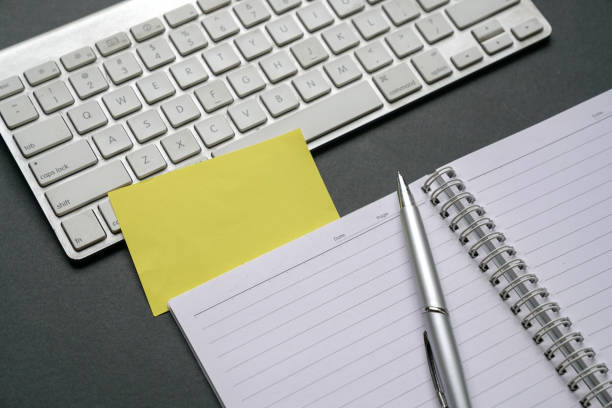 istock Top view of office table with computer keyboard, notepad, pen and blank yellow paper. 1253139112
