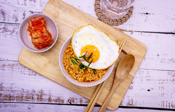 istock Spicy ramen (noddle) on a wooden board with side dish (Kimchi). 1253141574