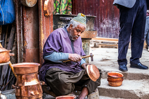 Local artisan pounding on copper pot and creating handmade dishes in old Medina market. Fes, Morocco - April 10 2016.