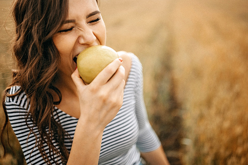 Young women enjoying summer in meadow and eating apple