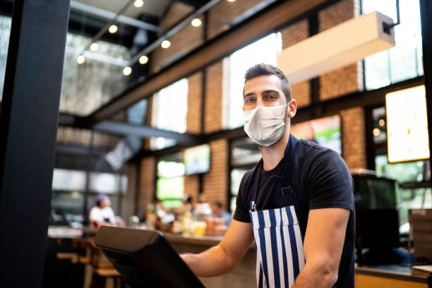 Portrait of a waiter typing on cash register using protective mask Portrait of a waiter typing on cash register using protective mask retail clerk photos stock pictures, royalty-free photos & images