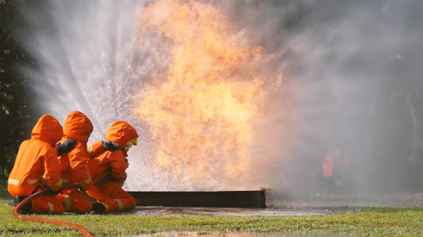 istock Firefighter fighting with flame using fire hose chemical water foam spray engine. Fireman wear hard hat, body safe suit uniform for protection. Rescue training in fire fighting extinguisher 1253165604