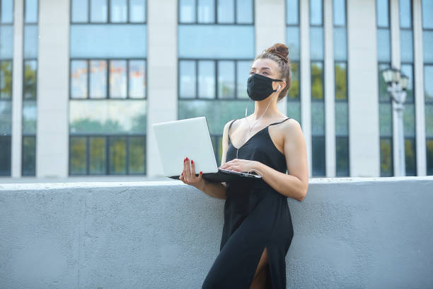 belle fille dans un masque se promène autour de la ville, travaillant sur un ordinateur portable. tenir un ordinateur portable et écouter de la musique - looking off camera photos et images de collection